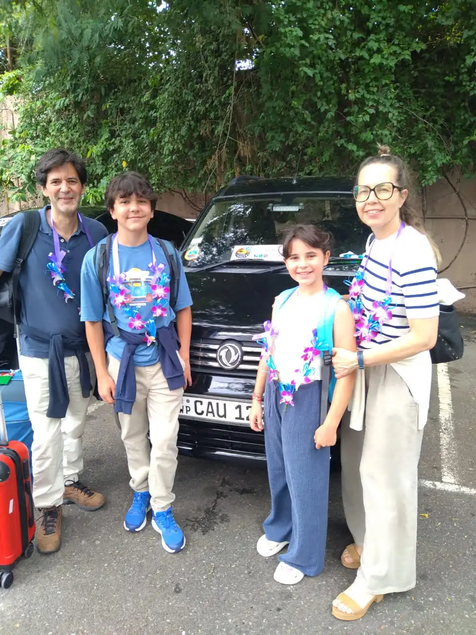 Family tourists with professional Sri Lankan driver outside accommodation - Happy group with Wego Taxi Tours guide and white vehicle at guesthouse